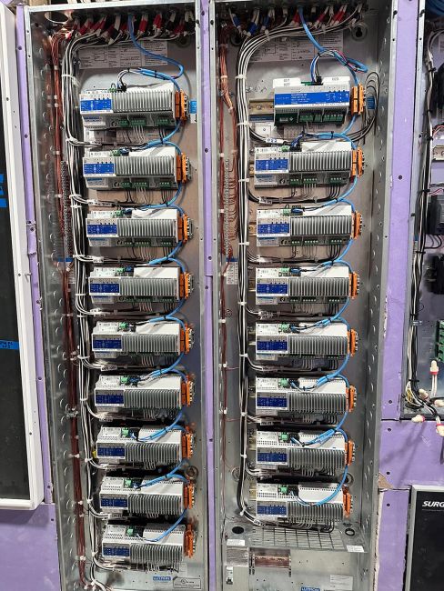 Parallel electrical panels neatly wired with white and blue cables inside a purple wall
