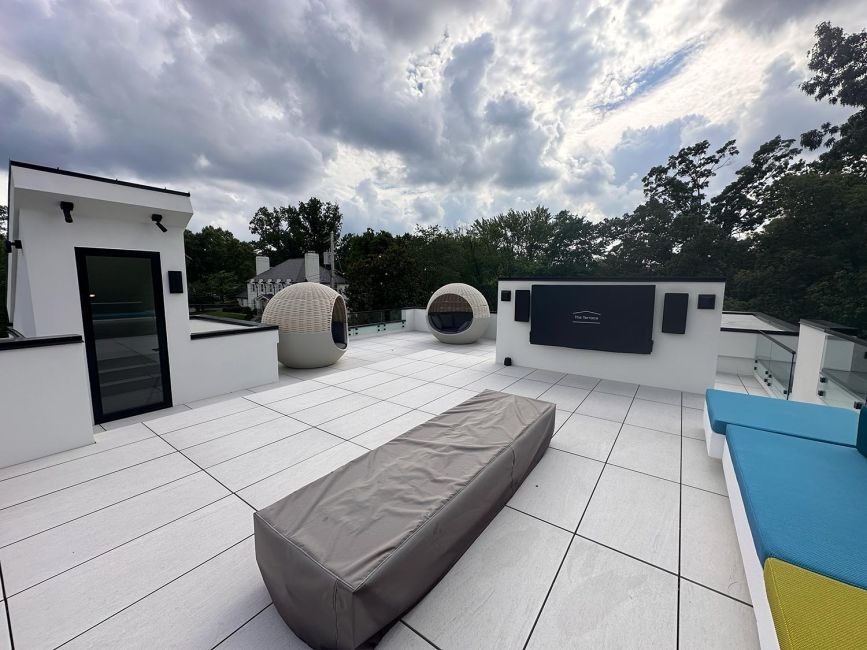 Expansive rooftop deck with stone tiles, modern outdoor furniture, and surrounding trees