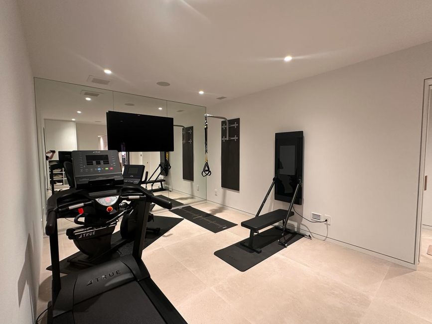 Home training room gym setup with a treadmill, lifting bench, and mirror wall panels
