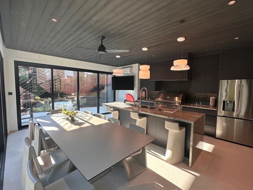 Open plan kitchen layout with long dining table next to wall-sized sliding glass doors
