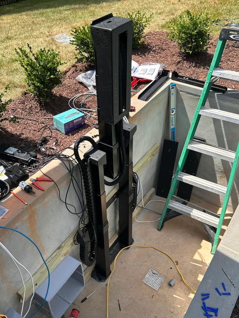 The mechanical assembly of a motorized outdoor hidden TV lift system being wired and installed inside its subterranean concrete enclosure.
