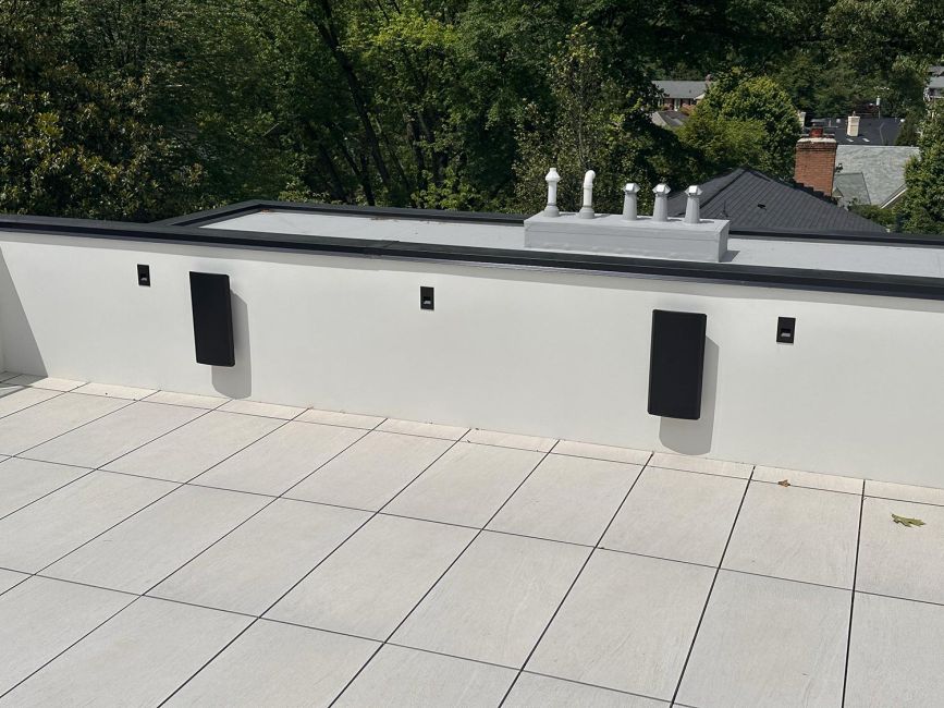 Rooftop tiled deck with modern black speakers mounted to white parapet wall
