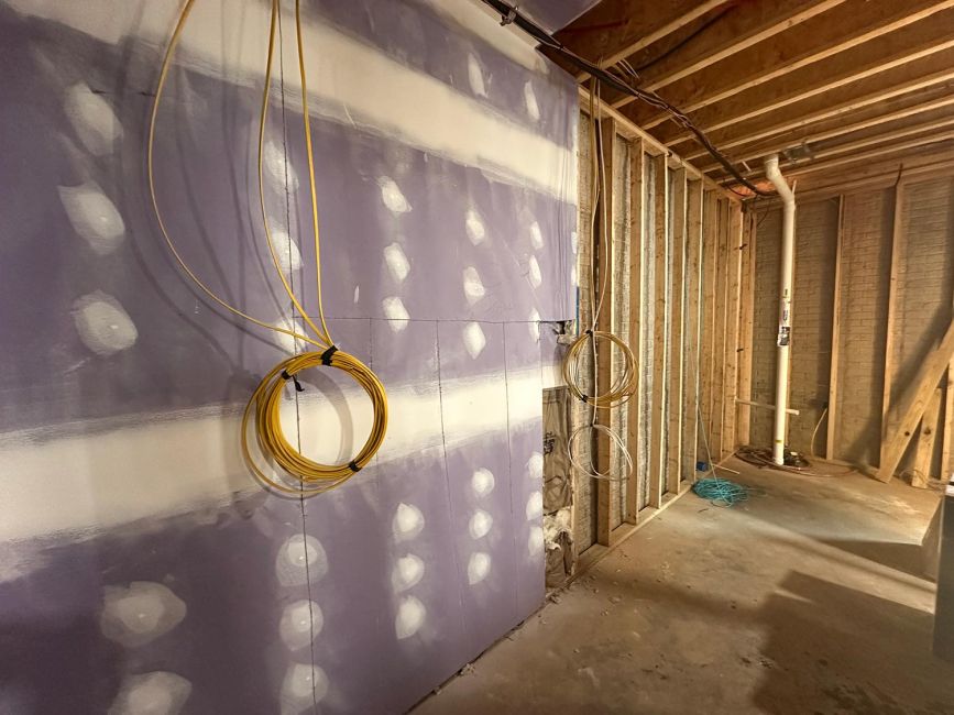 Coils of yellow wire hanging from a purple drywall surface in an unfinished room
