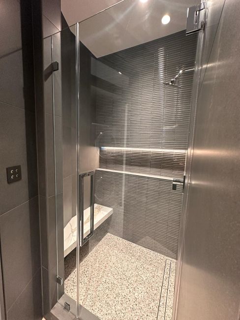 Walk-in shower featuring gray stacked horizontal tiles, a built-in bench, and glass door