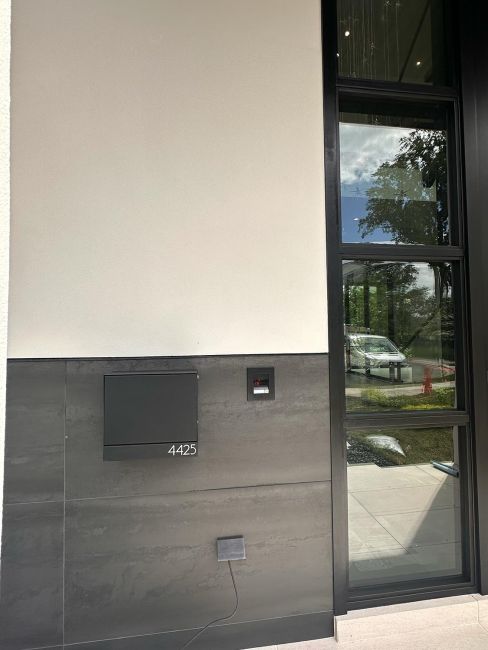 Modern home exterior entrance featuring wall mailbox and a tall glass door assembly